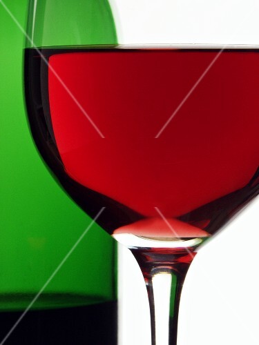 Red wine glass in front of red wine bottle (close-up)