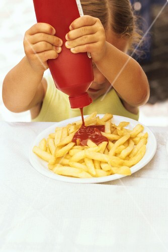 Mädchen drückt Ketchupflasche über Pommes aus