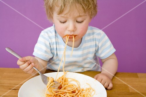 Kleiner Junge mit Spaghetti im Mund