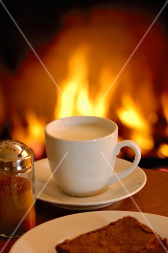 Eine Tasse Cappuccino vor brennendem Kamin-Feuer