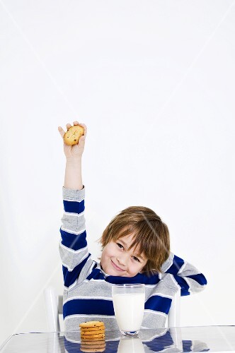 Boy with outstretched arm at table with cookies and milk