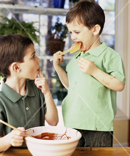 Two boys licking chocolate cake mixture