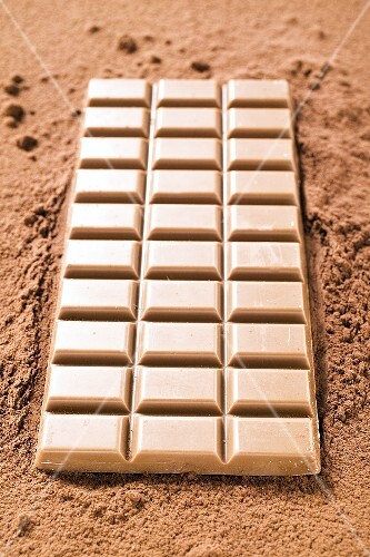 A bar of milk chocolate on cocoa powder