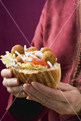 Woman holding flatbread filled with falafel (chick-pea balls)