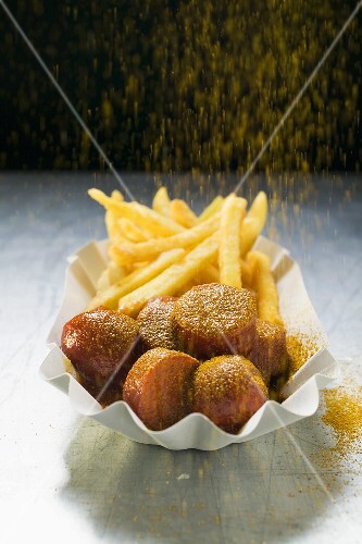 Sprinkling curry powder onto currywurst and chips