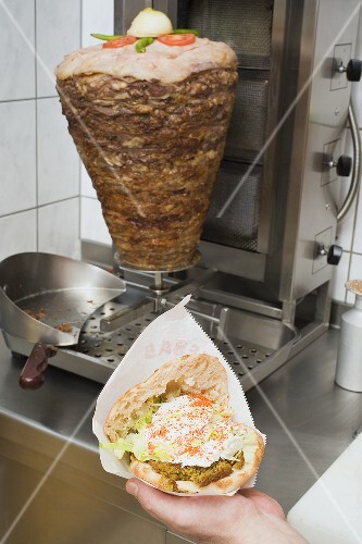Hand holding opened döner kebab in front of spit