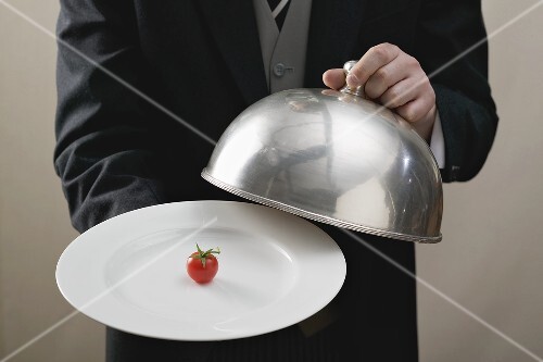 Butler serviert Kirschtomate auf Teller mit Cloche