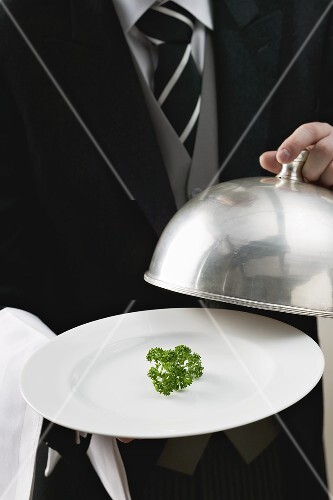 Butler serviert frische Petersilie auf Teller mit Cloche