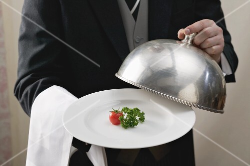 Butler serviert Tomate und Petersilie auf Teller mit Cloche