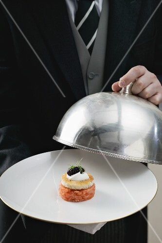 Butler serviert Lachstatar auf Teller mit Cloche