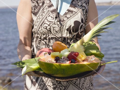 Woman holding tray of fresh exotic fruit by sea
