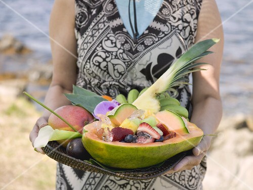 Woman holding tray of fresh exotic fruit by sea