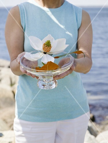 Woman holding glass dish of flowers, sea in background