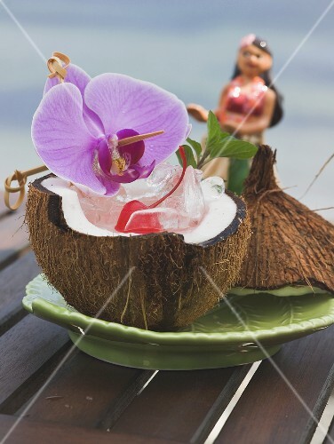 Half a coconut with ice cubes, cocktail cherry and orchid