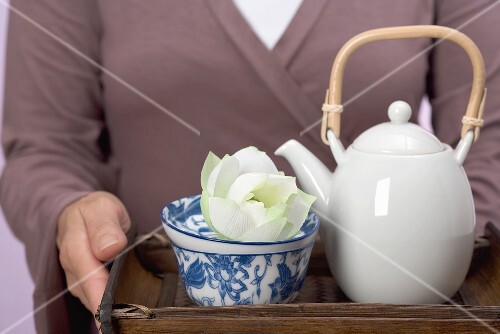 Frau hält Tablett mit Teekanne, Teeschale und Blüte