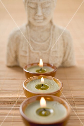 Three windlights in front of Buddha statue on bamboo mat