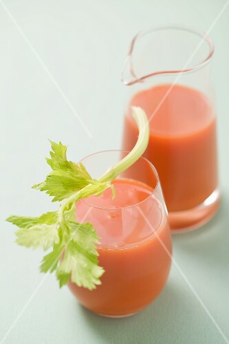 Glas Möhrensaft mit Staudensellerie, Krug im Hintergrund