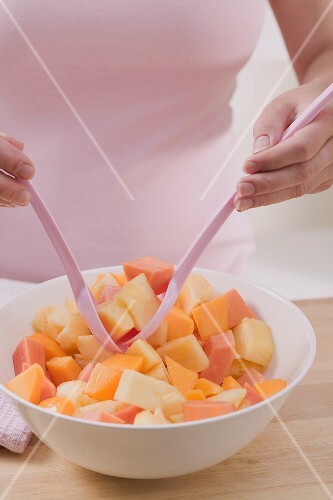 Woman taking fruit salad out of bowl with salad servers