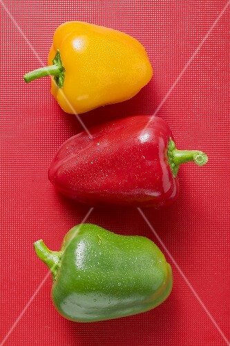 Different coloured peppers with drops of water on red background