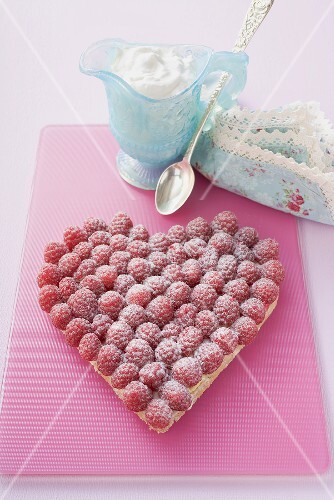 Raspberry tart with icing sugar, whipped cream in small jug
