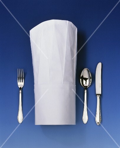 Chef's hat lying between knife, spoon and fork