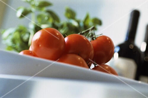 Tomatoes on kitchen table, basil and wine in background