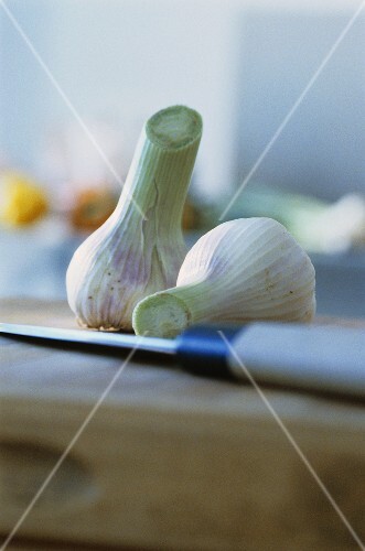 Two fresh garlic bulbs on chopping board with knife