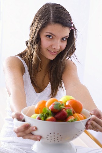 Girl holding a kitchen sieve with fresh fruit