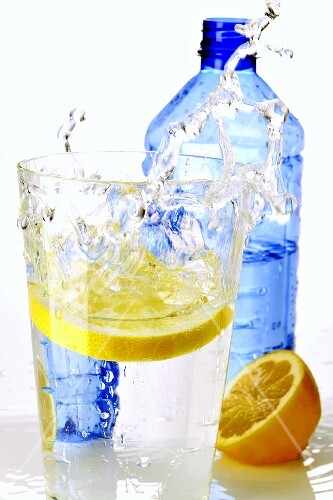 Zitronenscheibe fällt in ein Wasserglas