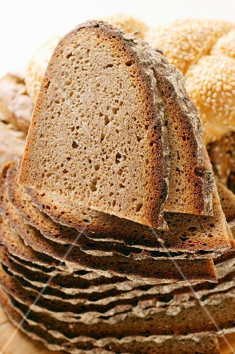 Slices of farmhouse bread in a pile in front of assorted rolls