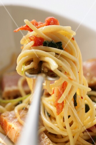 Spaghetti with tuna, tomatoes and basil on fork
