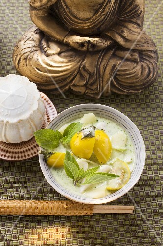 Kokossuppe mit Fisch und Thaiauberginen vor Buddhastatue