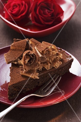 Piece of chocolate cake with chocolate curls, red roses