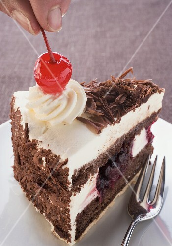 Decorating a piece of Black Forest gateau with cherry