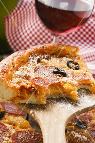 Stück Pizza mit Salami, Käse und Oliven (angebissen)
