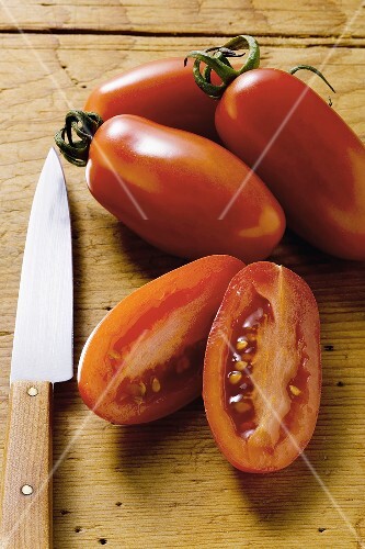 Vier Datteltomaten auf Holzuntergrund, eine halbiert