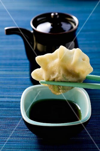 Pasta parcel on chopsticks above soy sauce