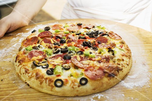 Hands holding pepperoni pizza with peppers and olives