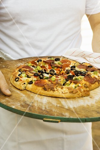 Person holding pepperoni pizza with peppers and olives