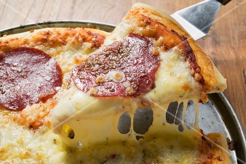 A slice of salami pizza being lifted up on server