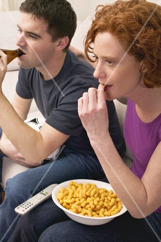 Young couple with football, beer and snack food watching TV