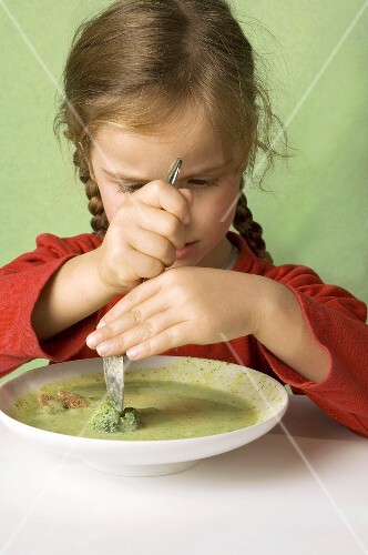 Girl cutting a broccoli floret in vegetable soup