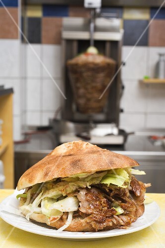 Ein Döner Kebab mit Fleischspiess im Hintergrund