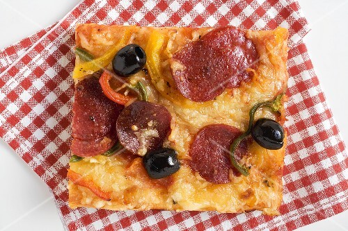 A slice of salami pizza with peppers and olives