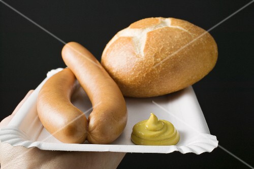 Sausages with mustard and roll on paper plate
