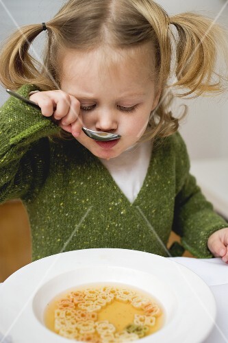 Small girl eating teddy bear noodle soup