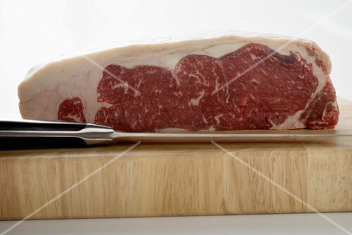 A piece of beef sirloin on wooden board with knife