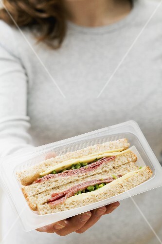 Woman holding two salami & cheese sandwiches in packaging