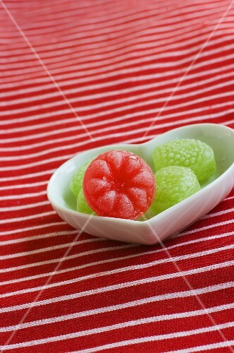 Green sweets and one red sweet in a heart-shaped dish