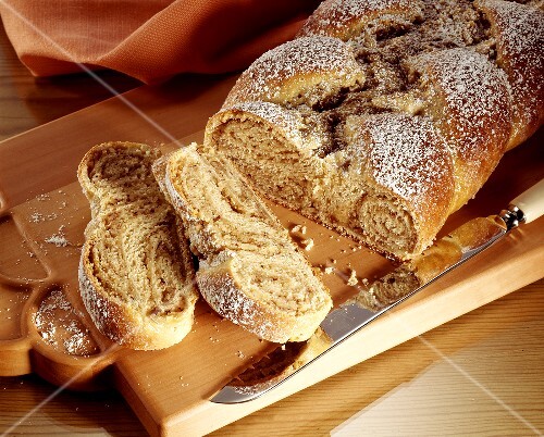 Nut plait sprinkled with icing sugar, pieces cut on wooden board